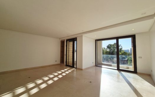 Grand salon baigné de lumière naturelle avec sol en marbre, baie vitrée panoramique ouvrant sur balcon avec garde-corps en verre et vue sur verdure, Ferme Bretonne Casablanca
