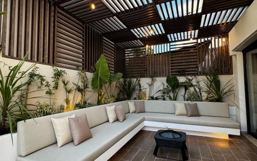 Terrasse couverte de 40m² avec pergola en bois, canapé d'angle extérieur, guirlandes lumineuses et végétation tropicale